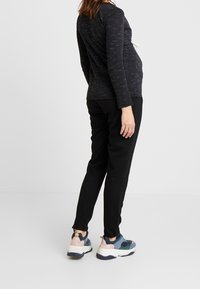 Svart långärmad topp med texturerade grå linjer, kombinerad med svarta byxor. Skorna har mångfärgade inslag och en klumpig suldesign.