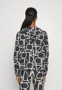 Kapuzensweatshirt aus schwarzem Stoff mit weißen geometrischen Mustern, langen Ärmeln und abgerundetem Saum, kombiniert mit passenden Leggings.