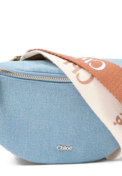 Jasnoniebieska półksiężycowa torebka z denimu z złotym suwakiem i logo „Chloé”, wyposażona w szeroki pleciony pasek w kolorze brązowym i kremowym z napisem „Chloé”.