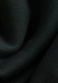 Nahaufnahme von schwarzem Stoff mit feiner Strickstruktur und sanften Falten, die Schatten und Lichtreflexe erzeugen.