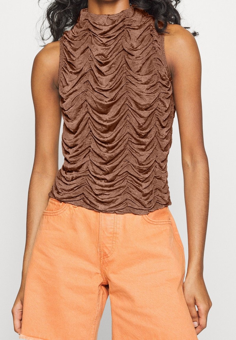 Brun ärmlös topp med hög hals, med en strukturerad plisserad design. Kombinerad med ljusorange denimshorts.