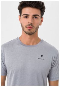 Grå kortærmet t-shirt lavet af blødt materiale, med rund halsudskæring og et lille sort logo på venstre brystområde.