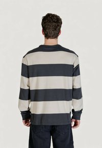 Camicia a maniche lunghe con righe orizzontali nere e beige, collo rotondo e vestibilità rilassata. Tessuto di cotone morbido con polsini a costine.