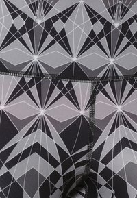 Černé a šedé legíny s geometrickým vzorem, který vykazuje ostré úhly a hvězdné motivy, vyrobené z elastického materiálu s hladkou texturou.