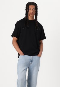 Tricou negru cu mânecă scurtă, în croială relaxată, asortat cu blugi de denim bleu deschis. Materialul pare moale, cu o textură netedă.