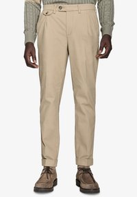 Beige bukser med et lige snit, plisseringer foran og knaplukning. Stoffet har tekstur, og der er opkrøllede manchetter, der fremhæver udseendet.