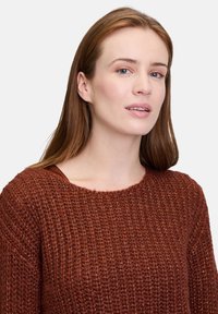 Maglione lavorato a maglia color ruggine con un motivo testurizzato, scollatura ampia e maniche lunghe. Materiale morbido con una leggera lucentezza.