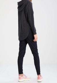 Felpa grigia scuro a maniche lunghe con orlo curvo e spacco laterale, abbinata a pantaloni blu con righe e sneakers rosa con suola bianca.