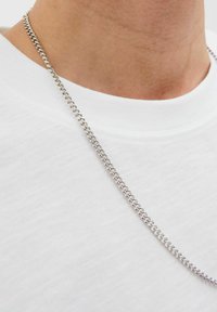 Silver chain necklace with polished links, resting on a textured white t-shirt neckline. Features a classic curb chain design.