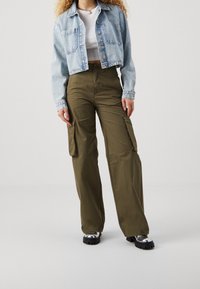 Ljusblått kort denimjacka med två framfickor, vit åtsittande topp och olivgröna cargobyxor med sidfickor. Svarta platåskor.