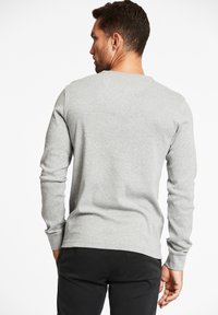 Grauer Sweatshirt mit langen Ärmeln, Rundhalsausschnitt und weichem Material. Über schwarzen Hosen getragen, zeichnet sich durch ein einfaches und klassisches Design aus.
