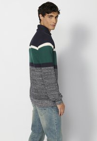 Sweter typu pulower z dzianiny w poziome pasy w kolorze granatowym, zielonym i białym, z wysokim kołnierzem i teksturowanym materiałem w odcieniach granatu i szarości.