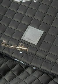 Tessuto grigio scuro trapuntato con un'etichetta a patch quadrata che riporta "name it" cucita al centro.