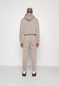 Beige hoodie with a drawstring and matching joggers. Soft fabric, relaxed fit, and a small pocket detail on the back of the pants.