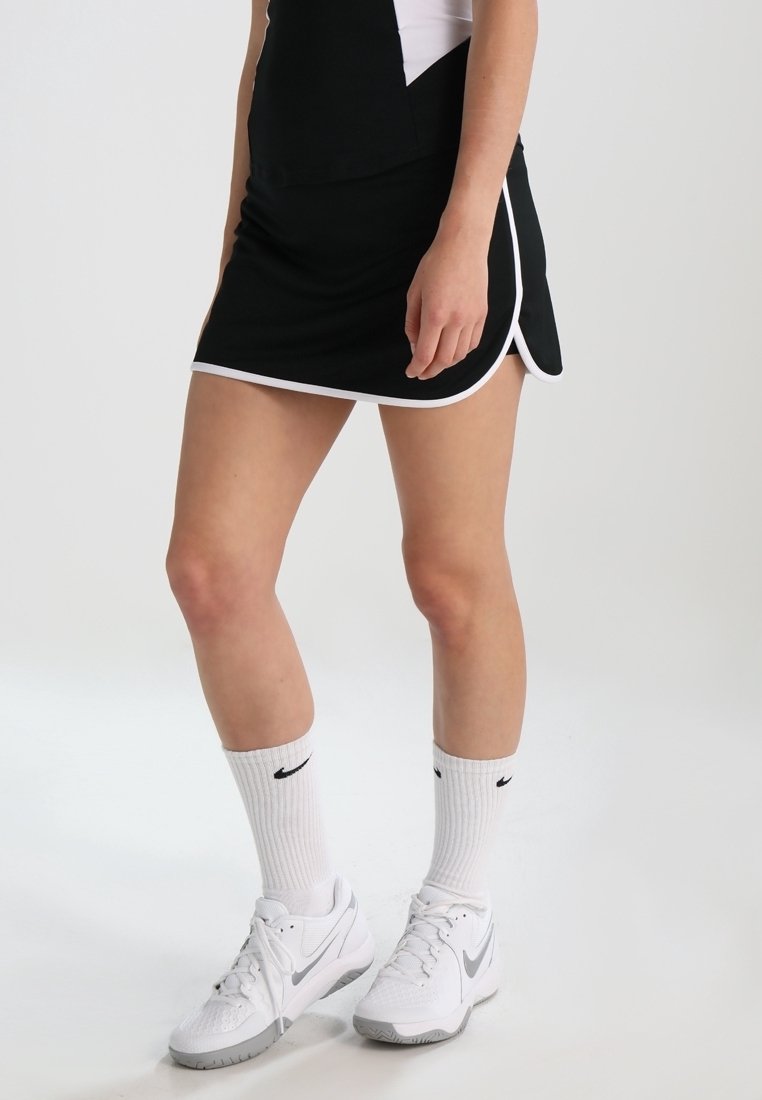 Černá sportovní sukně s bílým lemem, doplněná bílými ponožkami s černým logem a bílými sportovními botami se šedými akcenty.
