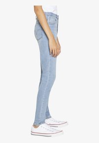 Light blue skinny jeans with a smooth texture, high waist, and back pockets, paired with white sneakers featuring colored accents.