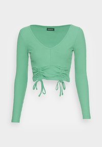 Top de manga longa verde menta canelado com decote em V e detalhes franzidos na cintura, apresentando cordões ajustáveis.