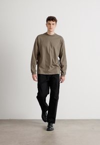 T-shirt en coton à manches longues, couleur olive, assorti à un pantalon cargo noir. Le modèle porte des chaussures noires. Coupe et style simples, décontractés.