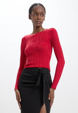 Top a maniche lunghe rosso a coste con un design aderente, caratterizzato da strisce verticali testurizzate, abbinato a una gonna nera con uno spacco laterale e vita annodata.