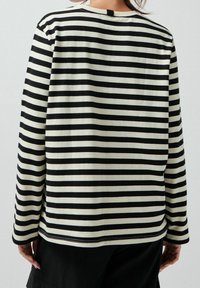 Takakats view of a person wearing a long-sleeve black and white striped shirt with black pants against a plain background.