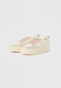 Platform sneakers in cream and light pink, featuring a suede toe cap, round laces, a padded collar, and a ridged rubber sole.