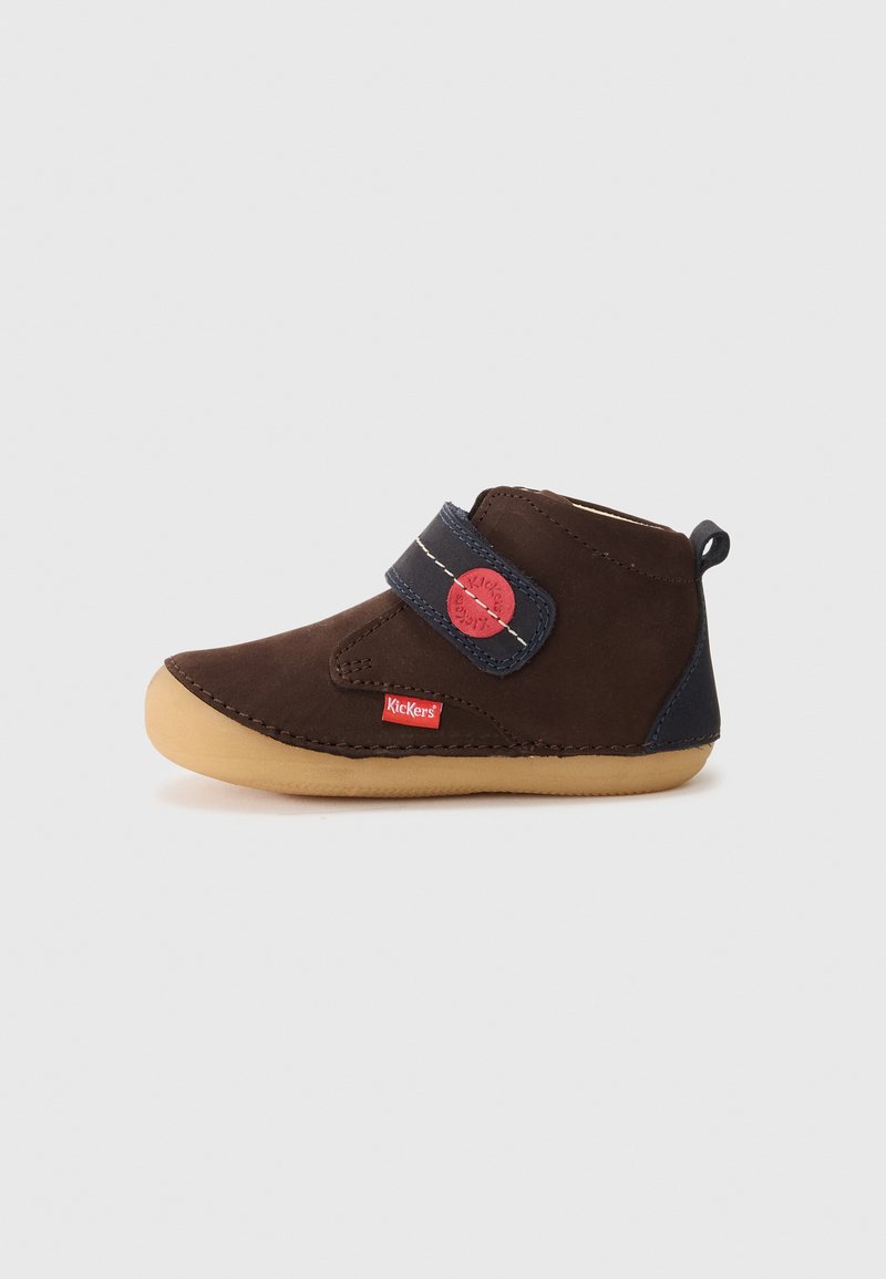 Scarpe Kickers per bambini in suede marrone con suola in gomma beige, fascia in velcro blu navy, etichette rosse con logo e linguetta sul retro, mostrate di lato.