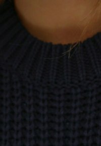 Dunkelblau gestrickter Pullover mit geripptem Kragen, der ein strukturiertes Muster aufweist. Nahaufnahme des Kragenbereichs mit einigen sichtbaren Haarsträhnen.