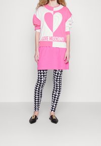 Rosa och vit tröja med en stor hjärtdesign och texten "LOVE MOSCHINO", parat med leggings med hjärt-mönster i svart och vitt samt svarta skor.