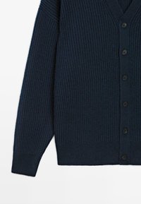 Mörkblå ribbad cardigan med V-hals, knäppning framtill och långa ärmar, tillverkad av ett strukturerat stickat material.