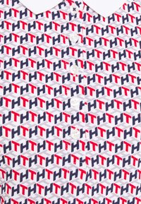 Short-sleeve polo shirt featuring a repeating geometric pattern in red, navy, and gray. Includes a white collar and three buttons.