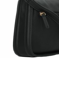 Bolso de mano de cuero negro con una textura suave, diseño angular, costuras en contraste y un cierre de cremallera en tono dorado. Se puede ver un compartimento lateral.