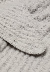 Tissu gris texturé avec une surface douce et duveteuse, présentant un col arrondi et un détail de bouton-pression argenté sur un côté.