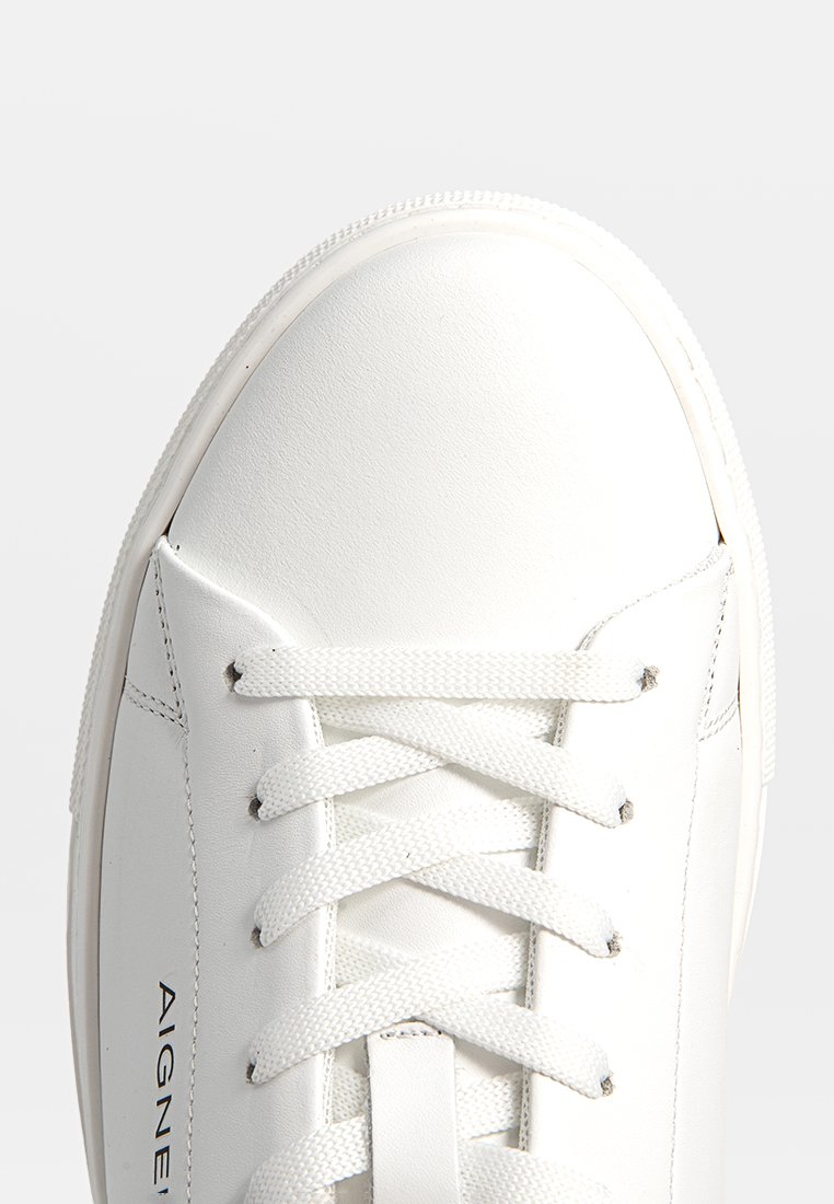 Sneaker bianco con tomaia in pelle liscia, puntale testurizzato e lacci piatti. Presenta un branding minimale in nero sul lato.