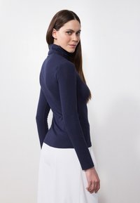 Sini turtleneck dengan lengan panjang yang slim fit, terbuat dari bahan lembut, dilengkapi dengan kerah tinggi dan detail jahitan di sisi.