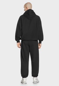 Czarny zestaw składający się z bluzy z kapturem i dresów, wykonany z miękkiego materiału; charakteryzuje się dużym kapturem, luźnym krojem oraz elastycznymi mankietami na kostkach.