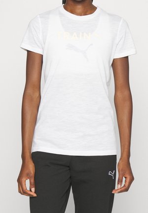 Osoba w białej sportowej koszulce Puma i czarnych spodniach Puma, stojąca ze swobodnie opuszczonymi ramionami.