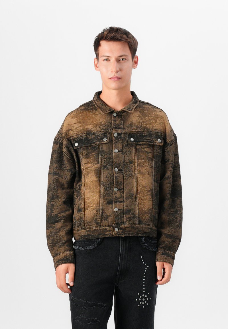 Iškblukusi ruda džinsinė striukė su mygtukų užsegimu, dviem krūtinės kišenėmis ir laisvu siluetu. Pabrėžta subtiliomis tekstūros variacijomis.