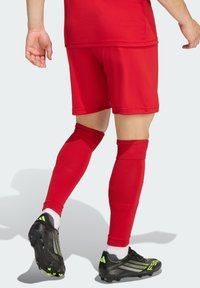 Κόκκινα ποδοσφαιρικά σορτς συνδυασμένα με κόκκινες κάλτσες μέχρι το γόνατο και μαύρα παπούτσια ποδοσφαίρου με πράσινες λεπτομέρειες. Λείο ύφασμα με εφαρμοστή σχεδίαση.