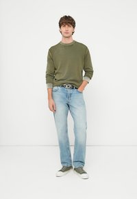 Olivovo zelený sveter s rebrovaným výstrihom, svetlomodré džínsy a sivé zelené tenisky; ležérny strih, textúrovaná látka a strieborná pracka na opasku.