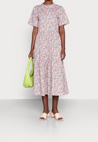 Vestido midi floral con mangas cortas en rosa, que presenta hojas verdes y flores. Se lleva con sandalias de tacón bajo color beige y un bolso verde lima.