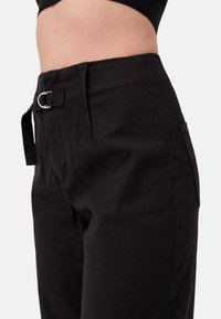 Zwarte linnen hoge taille broek met een zijzak, riemlussen en een zilveren gesp detail. Gelaagd stof met een ontspannen pasvorm.