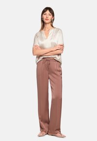 Seidenbluse mit V-Ausschnitt und kurzen Ärmeln; kombiniert mit locker sitzenden, mit Kordelzug verstellbaren Hosen in zartem Rosa; flache Schuhe. Durchgehend glatte Textur.