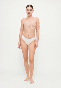 Spets-bh i ljusrosa med genomskinliga kupor och justerbara axelband, kombinerad med vita sömlösa bikini-trosor. Mjuk textur, minimalistisk design.