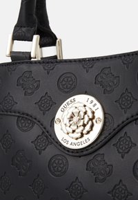 Zwarte handtas met structuur, voorzien van geperste bloemen- en logopatronen, zilverkleurige accenten en een decoratieve bloemvormige sluiting met merknaam.