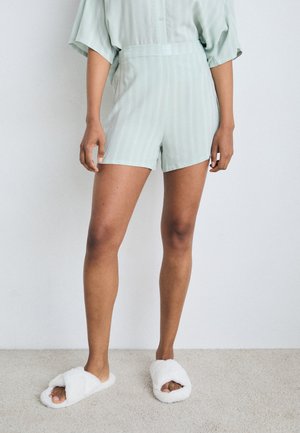 Shorts rayés vert clair avec une coupe décontractée et une taille plate. Associés à des chaussons moelleux blancs. Longueur courte atteignant le mi-cuisse.