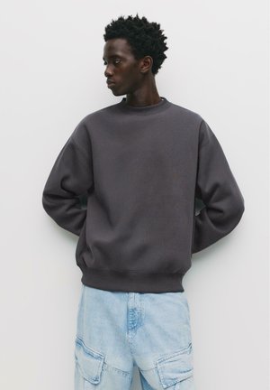 Šedá mikina s uvoľneným strihom, rebrovaným výstrihom a manžetami, kombinovaná so svetlomodrými cargo nohavicami s viacerými vreckami.