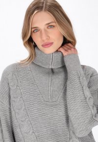 Pulover gri tricotat, cu guler înalt și fermoar, modele texturate și detalii cu torsade pe mâneci.