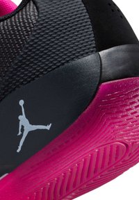 Zapatilla negra con parte superior texturizada, presenta una suela de goma rosa y un logo Jumpman gris. Se evidencian acabados suaves y mate.