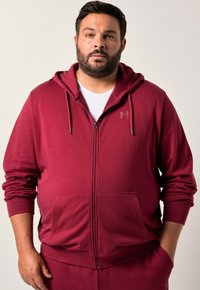 Felpa con zip di colore bordeaux realizzata in materiale morbido, con cappuccio, tasche anteriori e un logo discreto stampato sul petto.