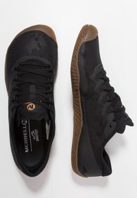 Czarne buty sportowe z siateczkową cholewką, gumową podeszwą z teksturowanym bieżnikiem i płaskimi sznurowadłami. Logo marki widoczne na języku.